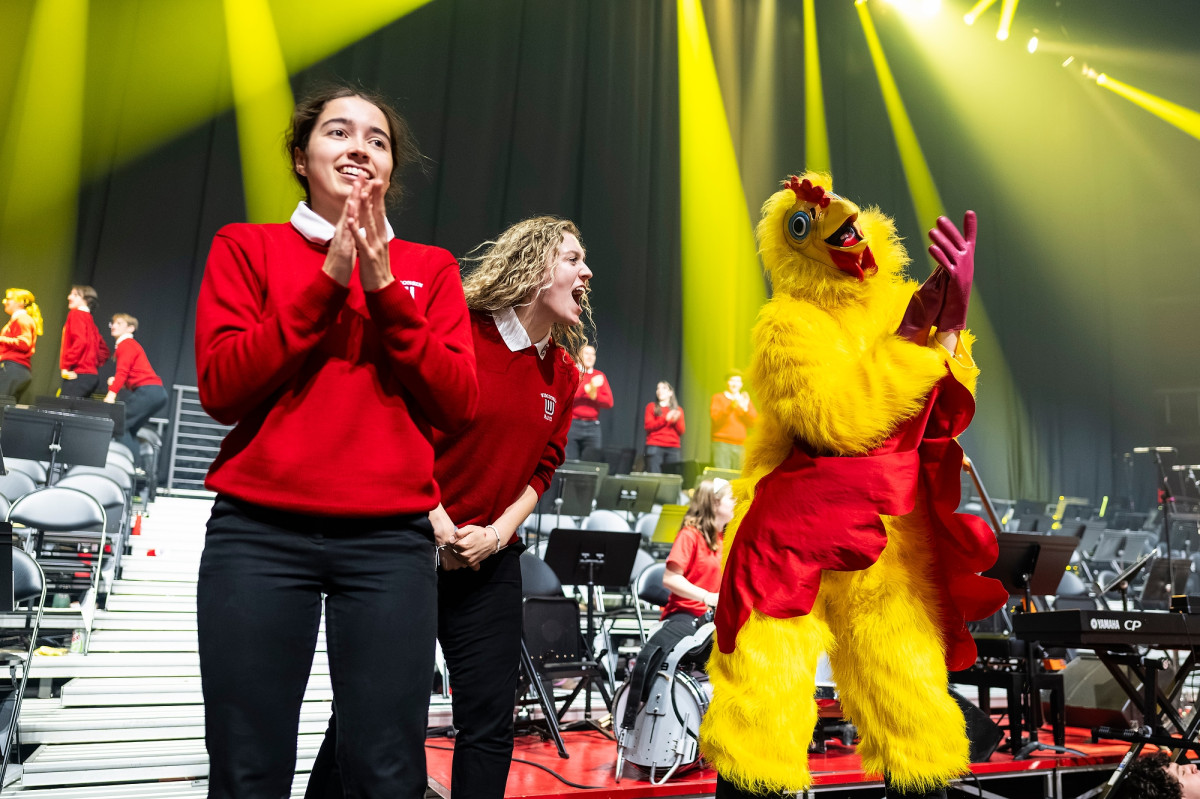 Two UW Marching Band members dance on stage with a person in a chicken costume.