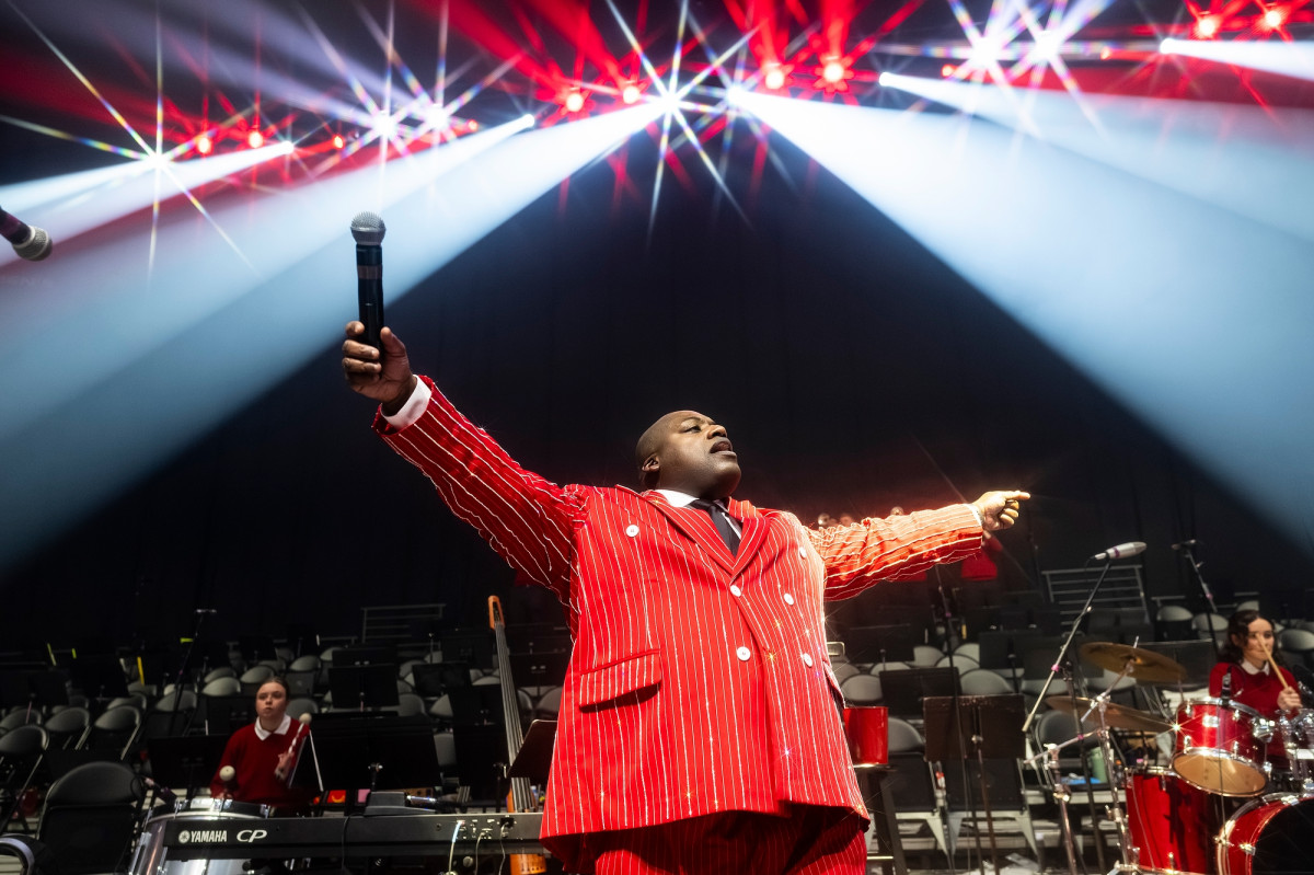 Pompey stands on stage wearing a Badger red suit with silver sparkly pinstripe as he conducts the crowd.