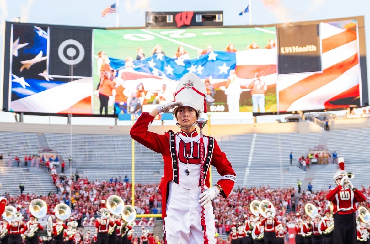 An assistant drum major saluting on the field during the national anthem at Camp Randall Stadium