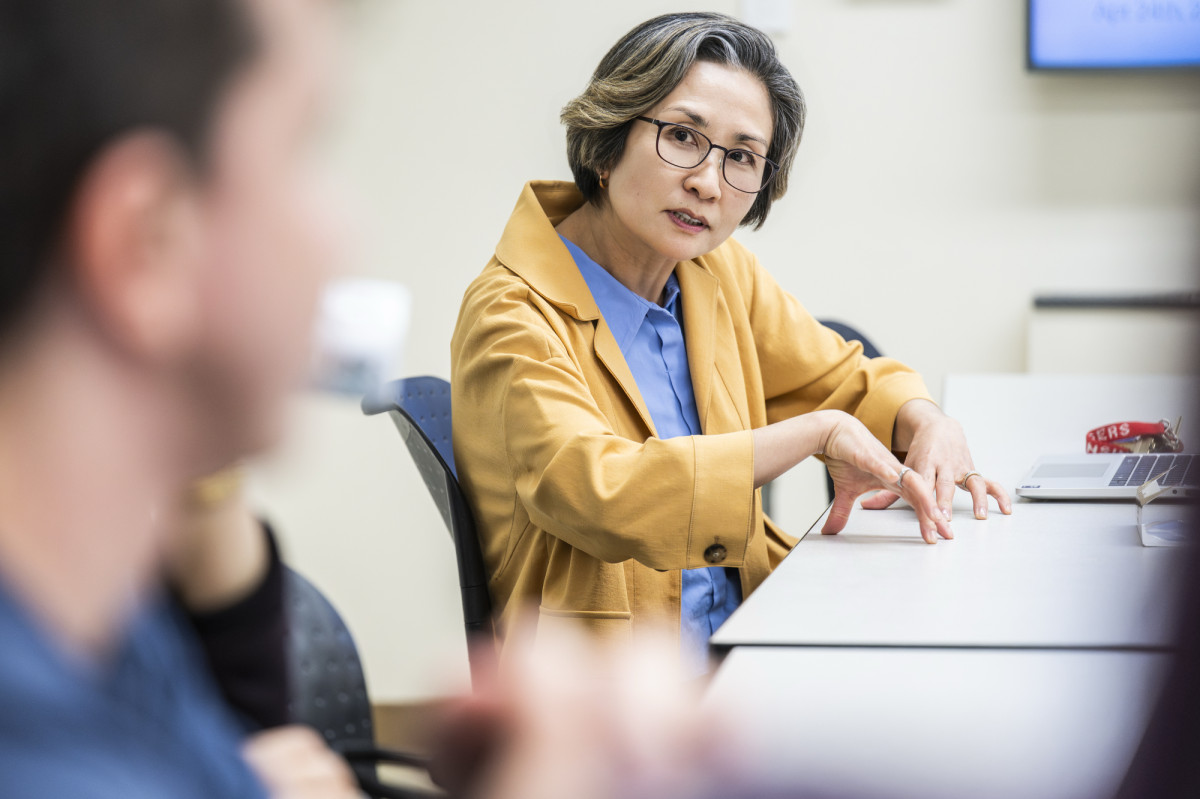 Jacee Cho sits at a long table while talking to a student and gesturing with her hands.