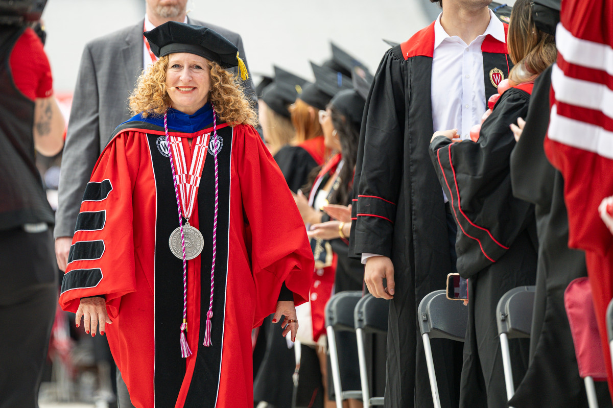 Mnookin, wearing academic robes, walks down an aisle, smiling, surrounded by others in commencement gowns.