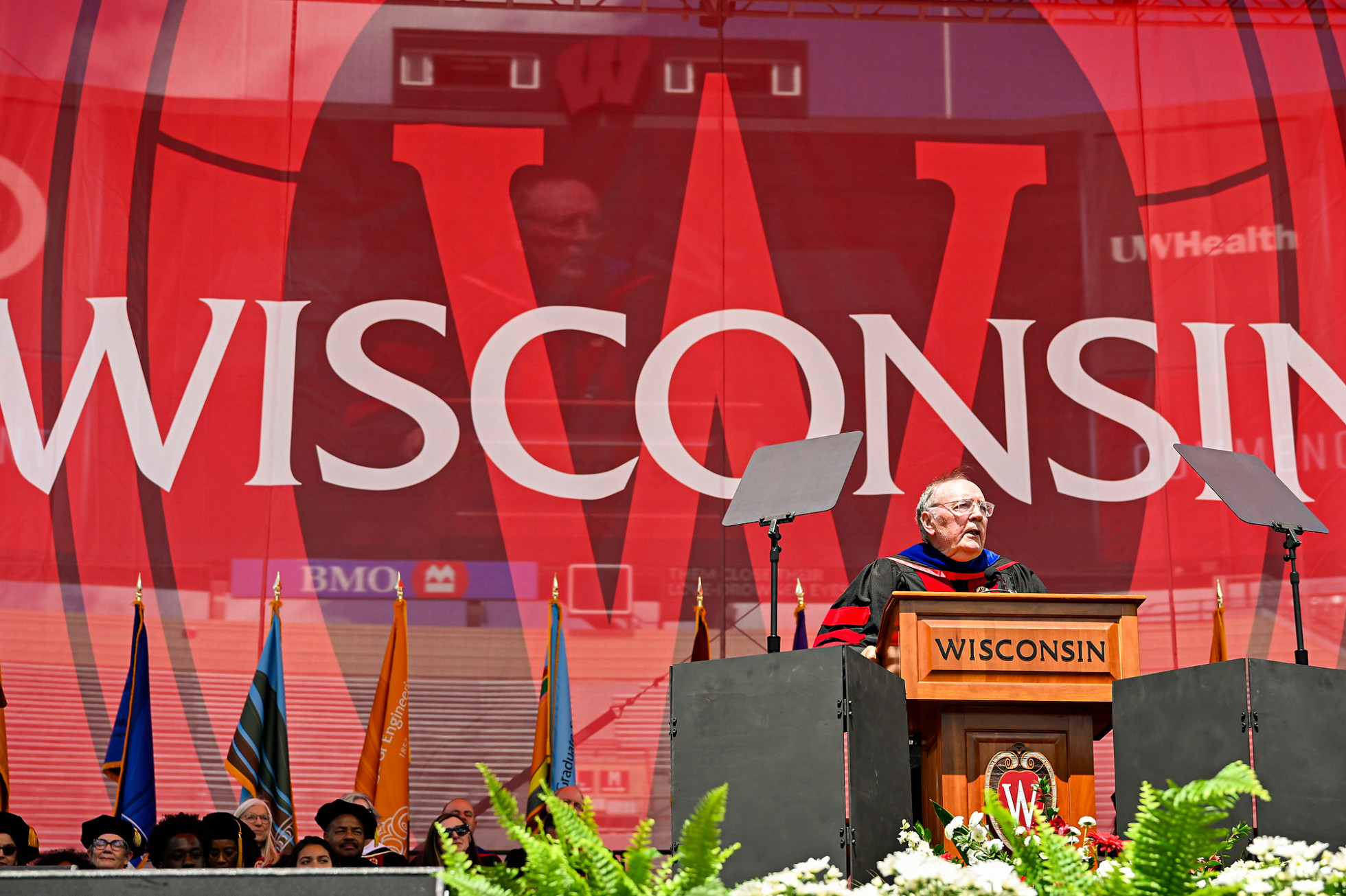 Patterson wears academic regalia speaks to the crowd from behind a podium.