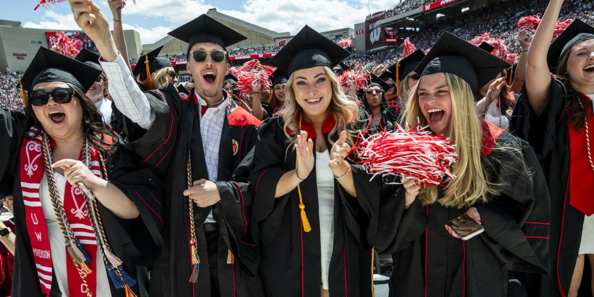 A group of enthusiastic graduates wearing their caps and gowns raise red and white pom-poms and jump in celebration.