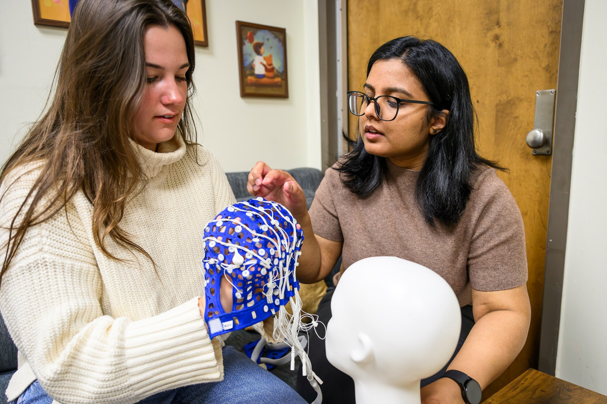 Aditi Gargeshwari works with an undergraduate research assistant holding an EEG cap.
