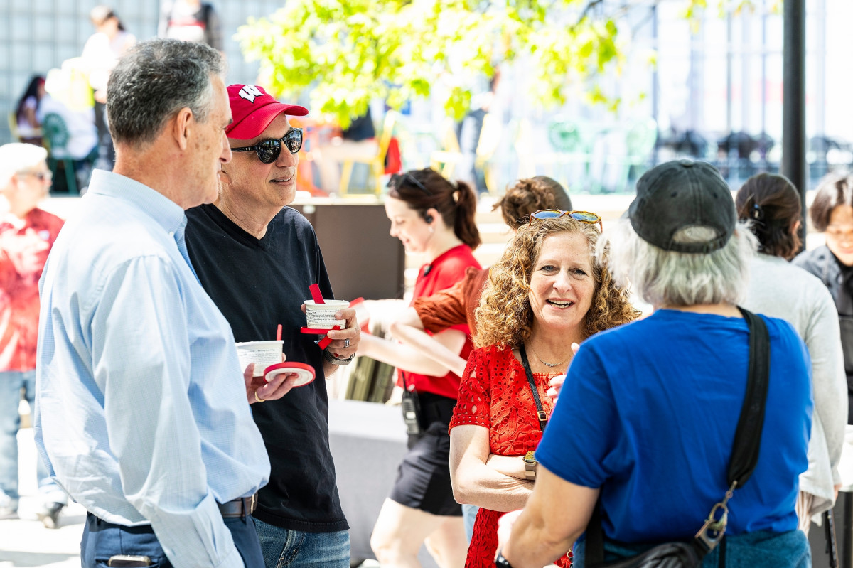 Mnookin, wearing a red dress, and Foa Dienstag, wearing a red UW Badger baseball hat, casually chat with event guests on the Memorial Union Terrace.