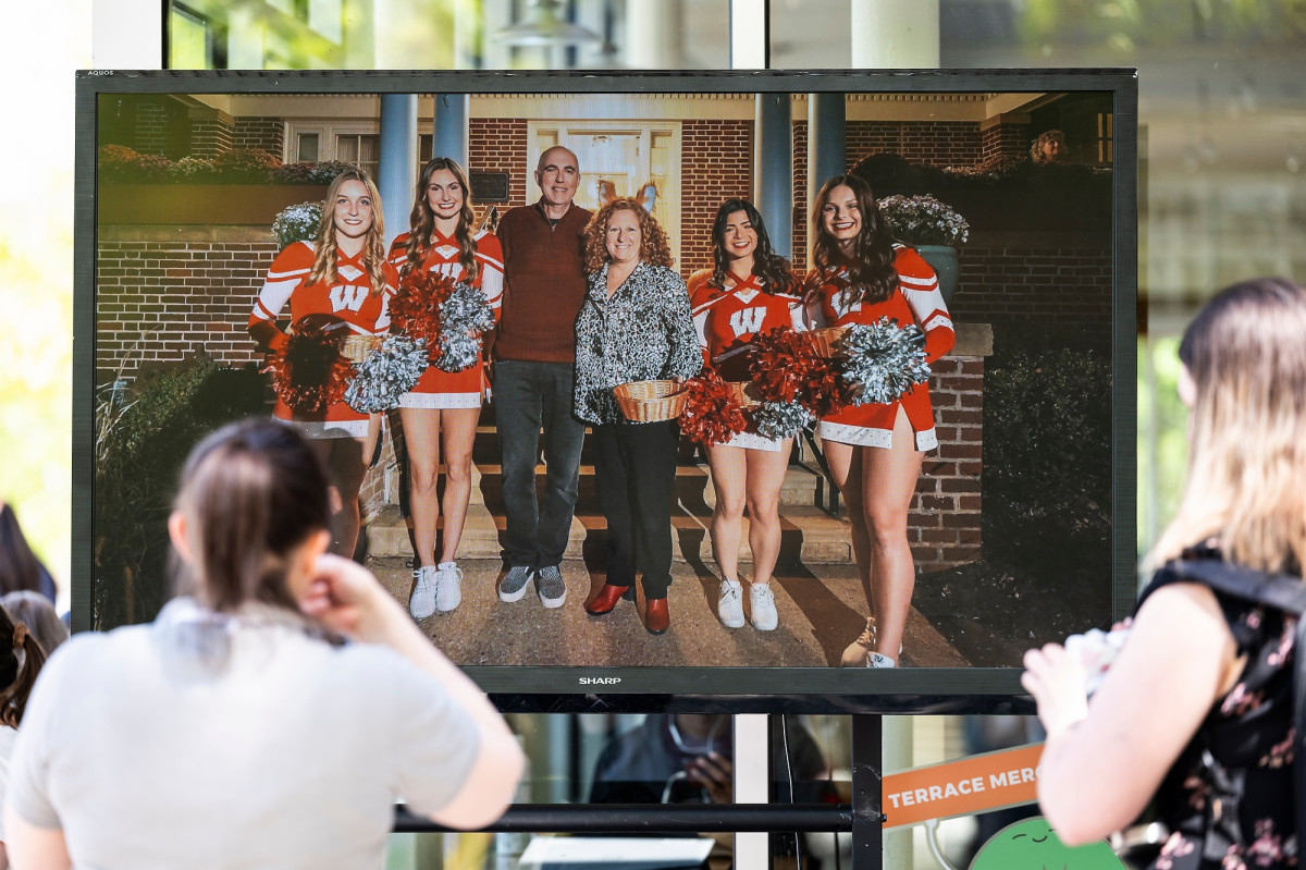 Guests stand in front of a large TV screen that displays a rotating gallery of photos of Chancellor Mnookin during her tenure at UW–Madison.