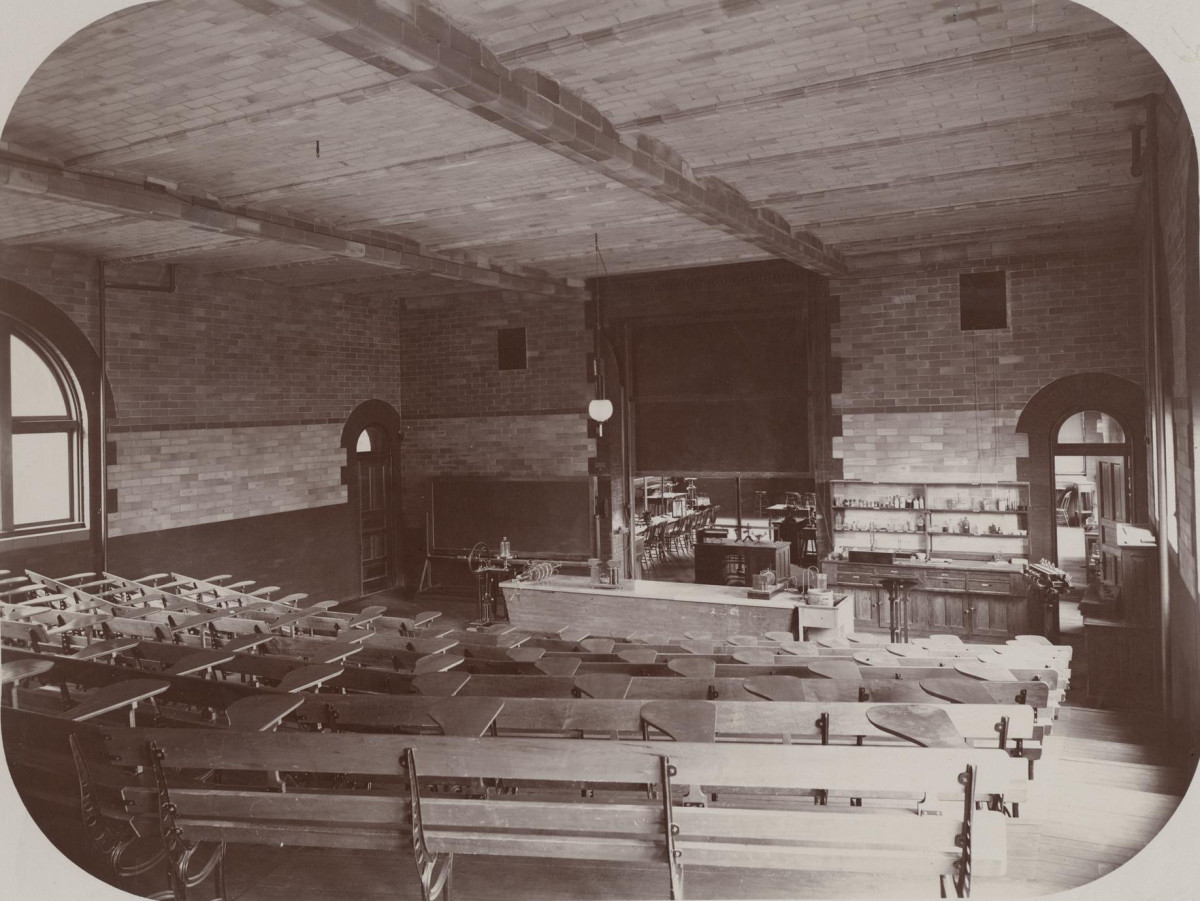 A black and white photo of an old lecture hall at UW–Madison. It shows rows of seats in a dimly lit brick room.