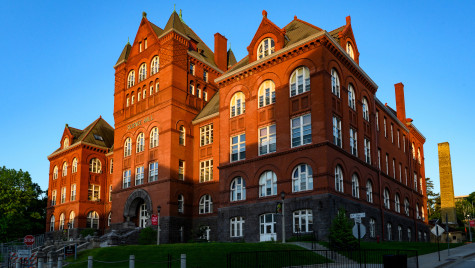A large red building with many white-framed windows. There is a shaft of sunlight cast across part of the building, which is set against a oure blue sky.