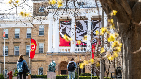 Two students with backpacks walk up Bascom Hill, with Bascom Hall and a Bucky Badger banner in the background.