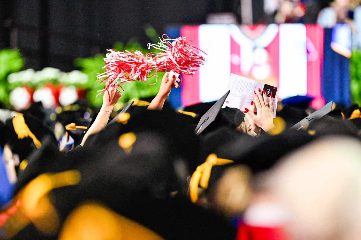 Graduates wave red-and-white pom-poms in the air.