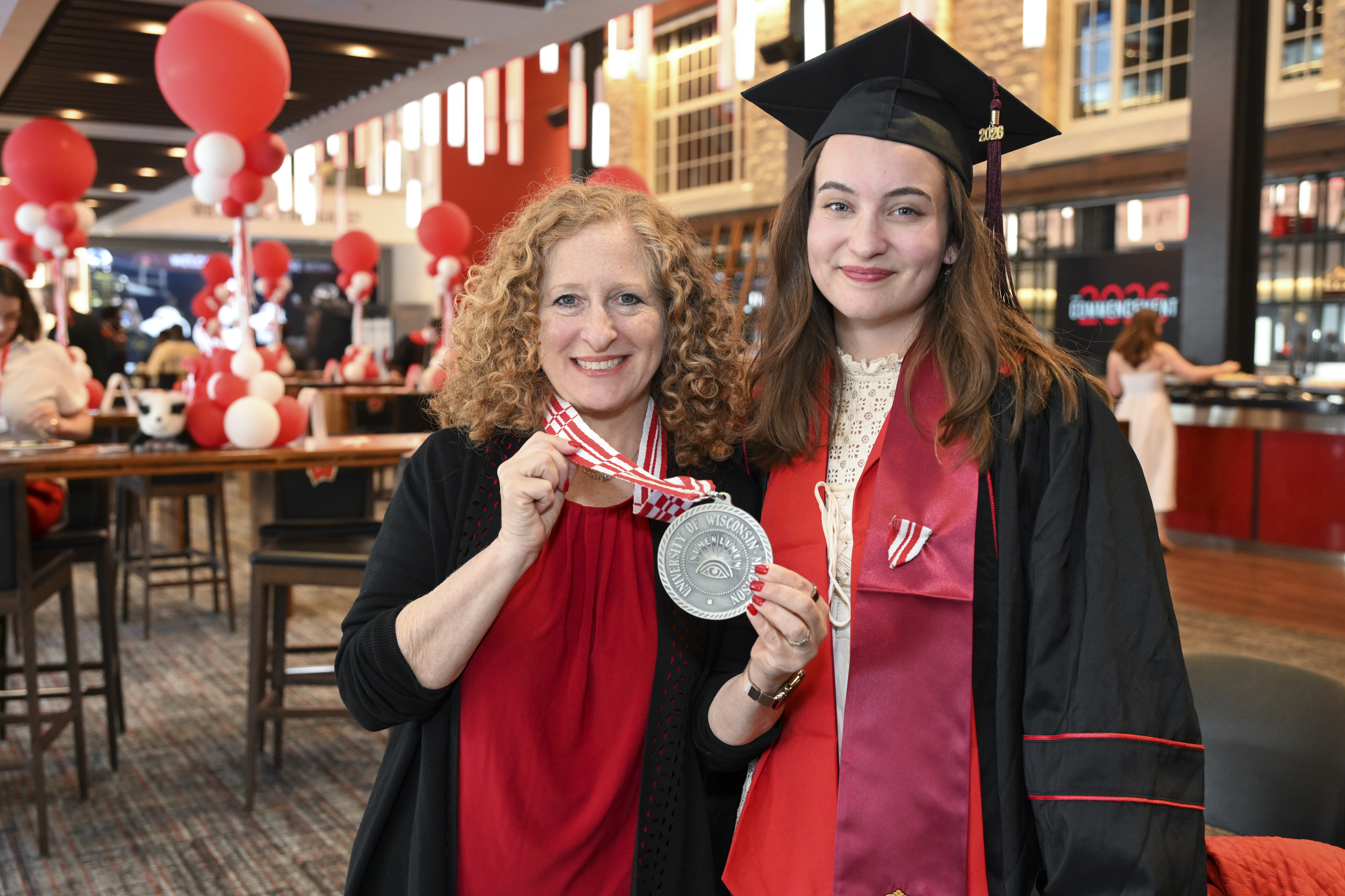 Mnookin holds up a gold medallion from her next while standing next to a cap and gown- clad Ambrosius