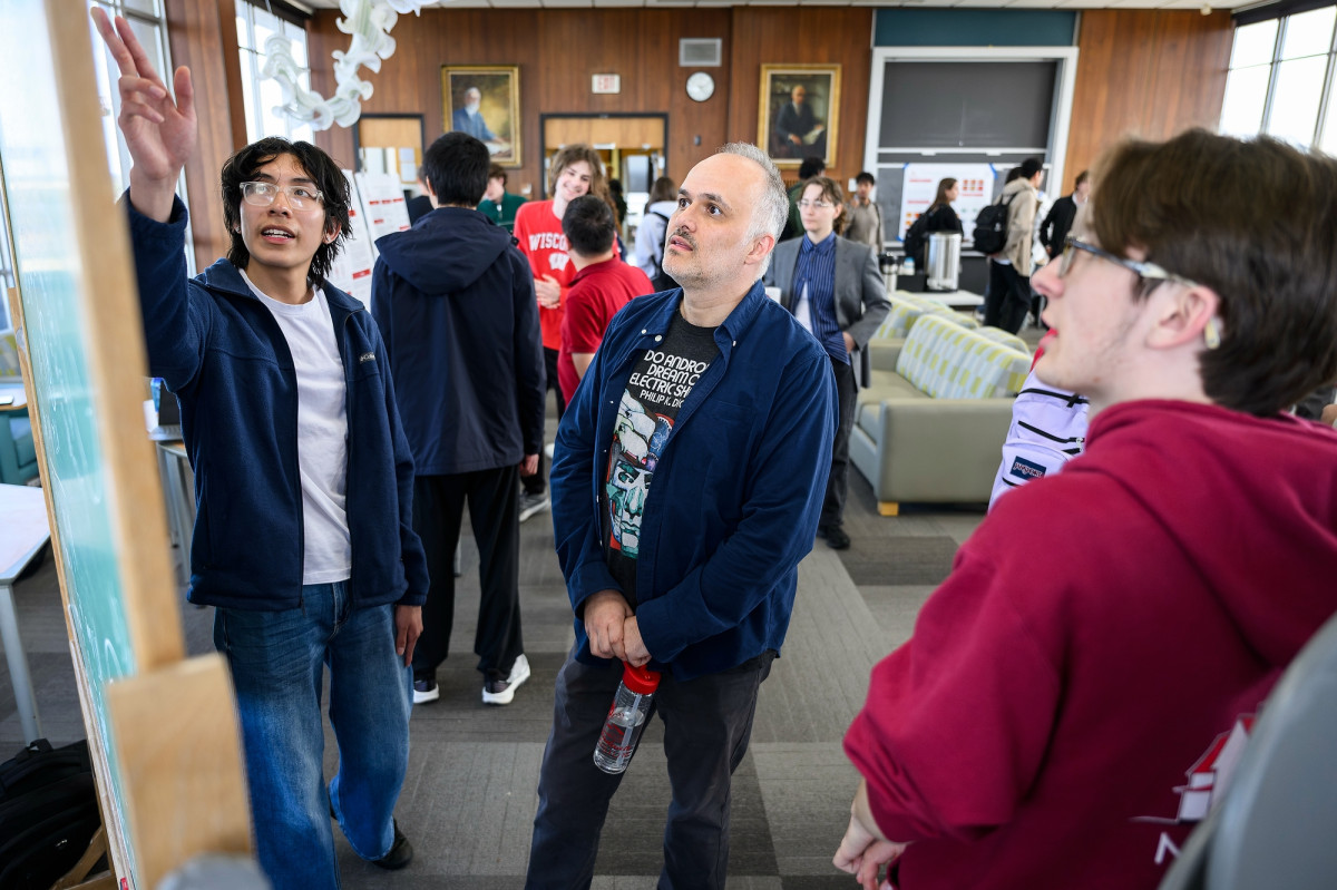Caglar Uyanik speaks with students and looks at their research poster at an open house.