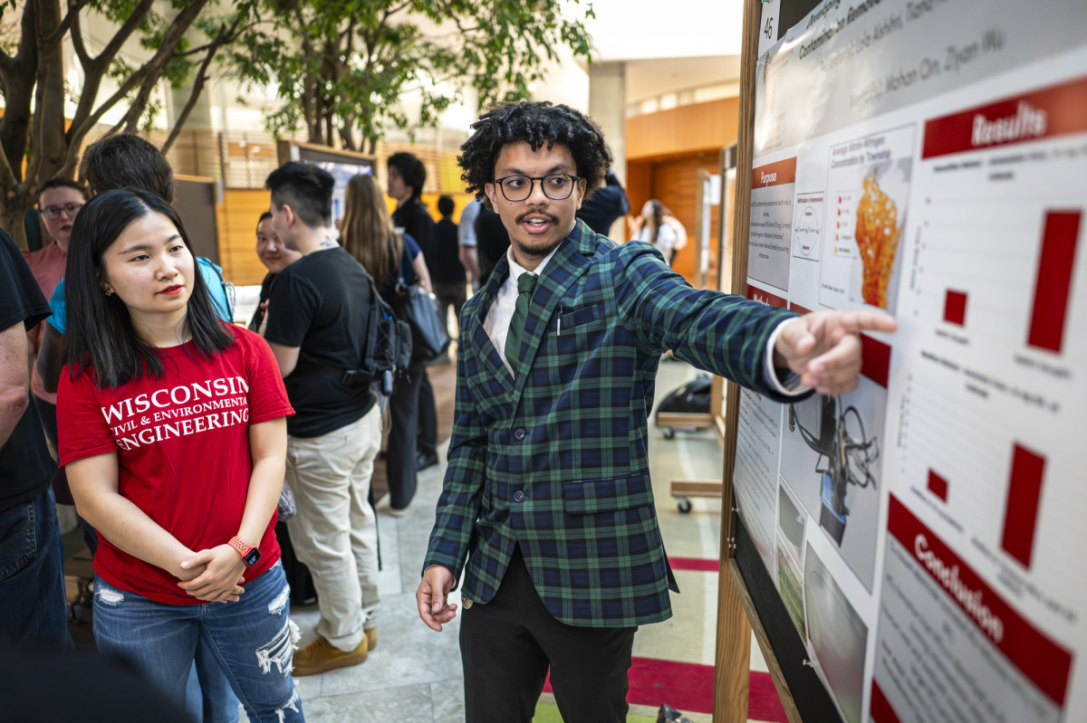 Ziyan Wu looks at a research poster that an undergraduate student is pointing to and explaining.