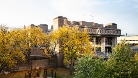 Large trees separate Vilas Hall in the background from the Divine Nine Plaza in the foreground.