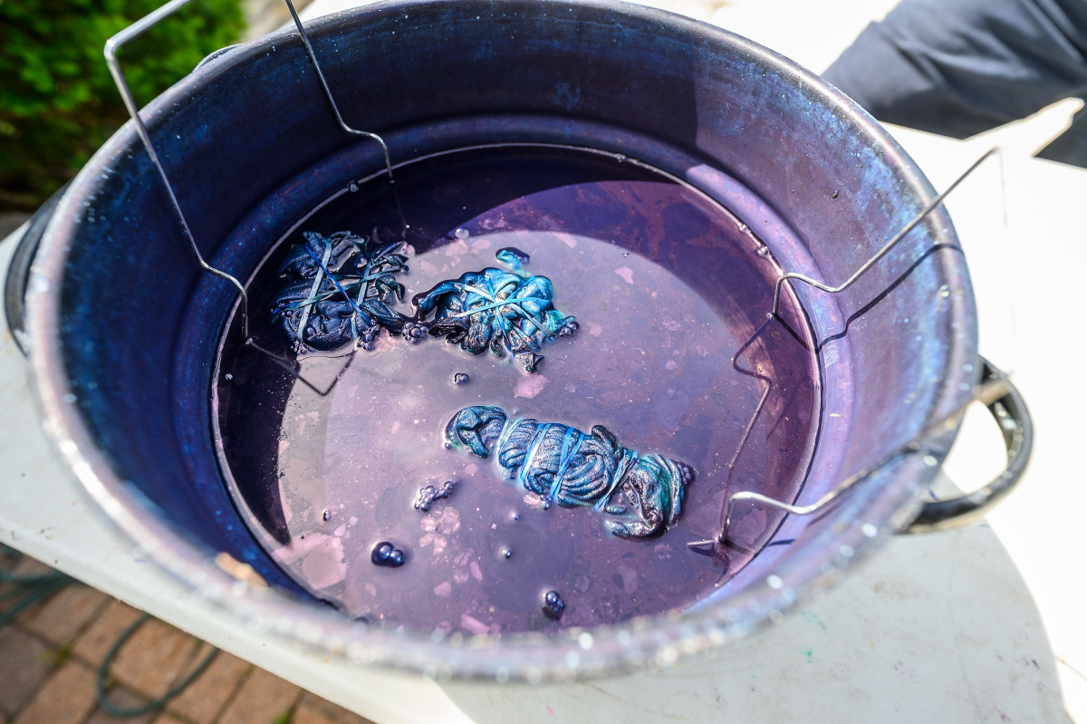 Three band-tied shirts sit in a pot filled with dark blue liquid.