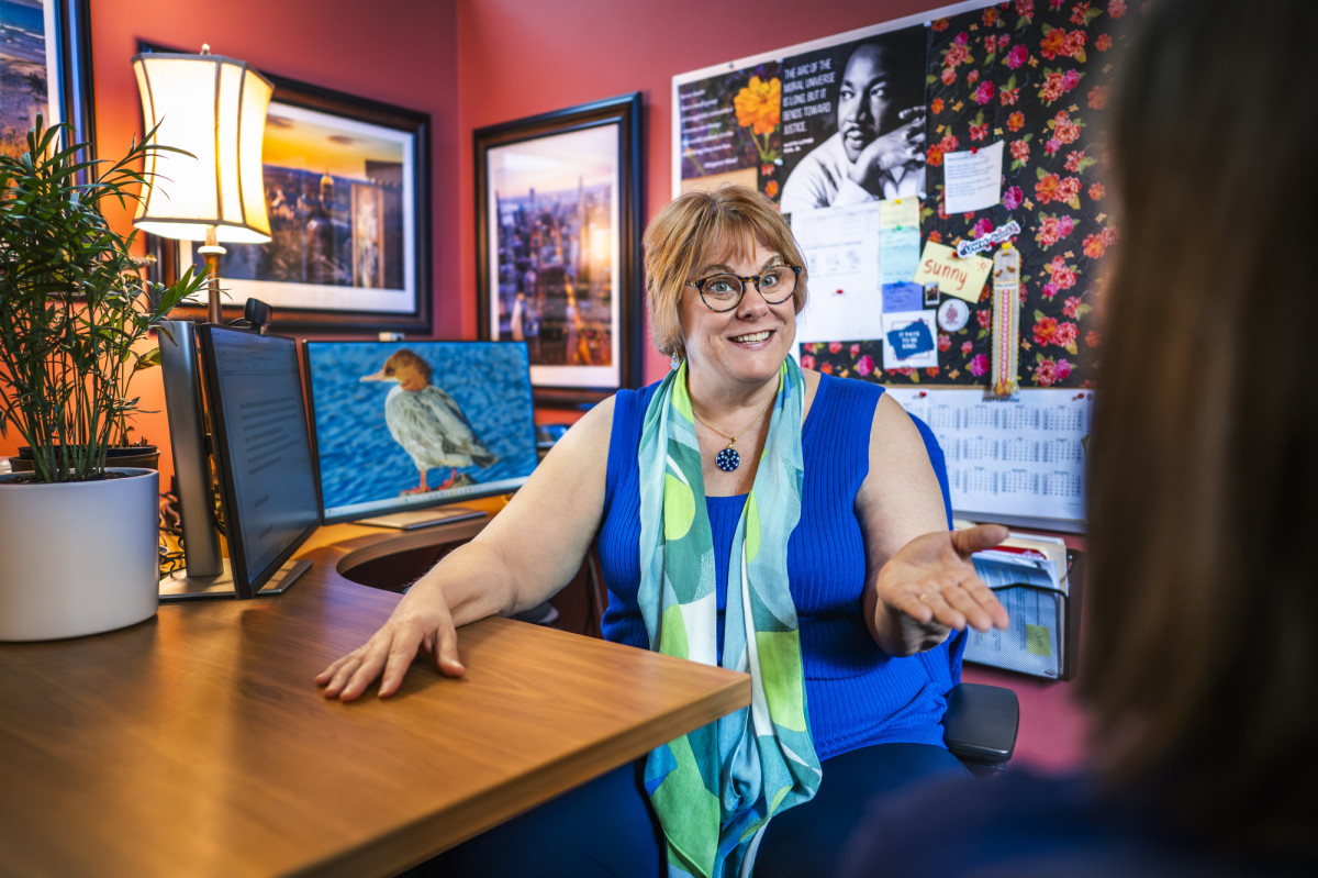 Carol Cizauskas sits at her desk with bright posters behind her on the wall.