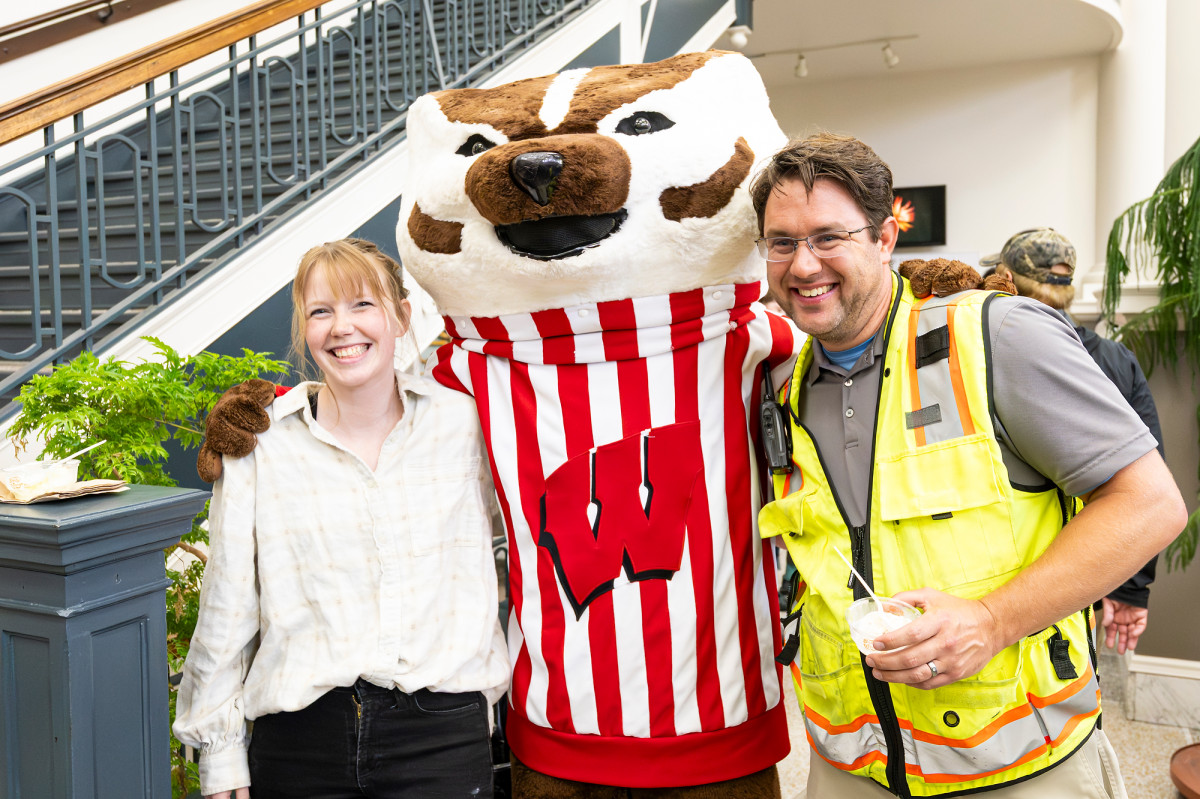 Mascot Bucky Badger poses with two employees.