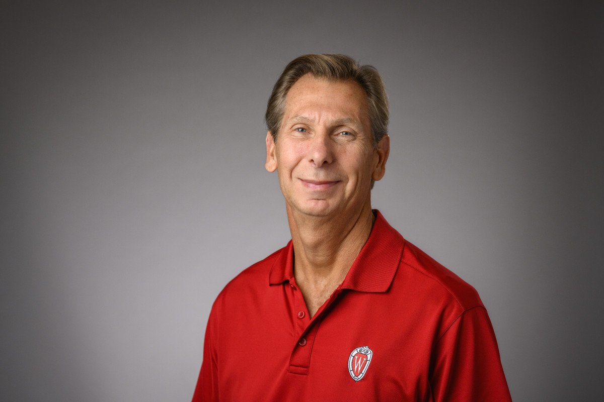 A portrait of Charles Hoslet in a red UW branded shirt in front of a neutral background.