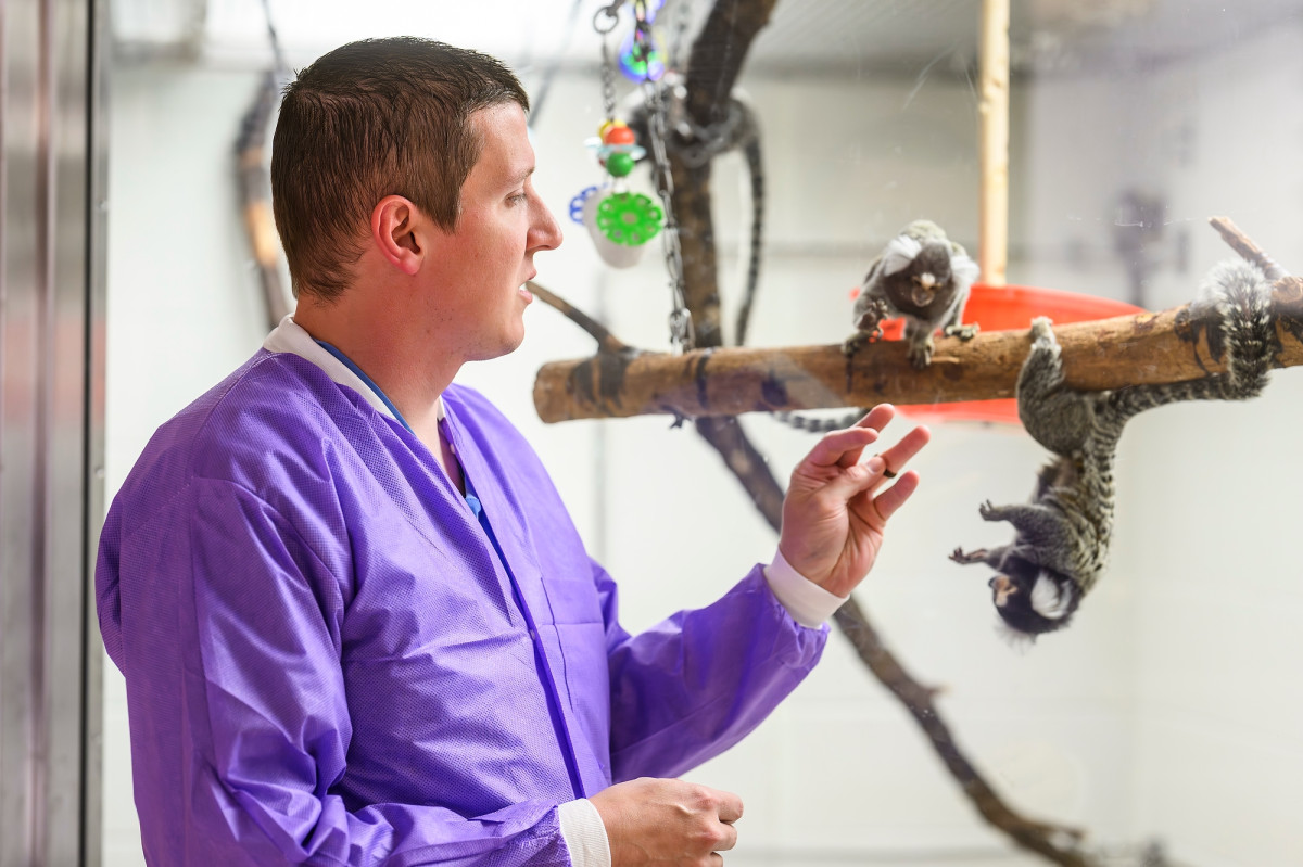 Cody Mortensen is shown at the Wisconsin National Primate Research Center standing next to a glass enclosure where animals are housed.