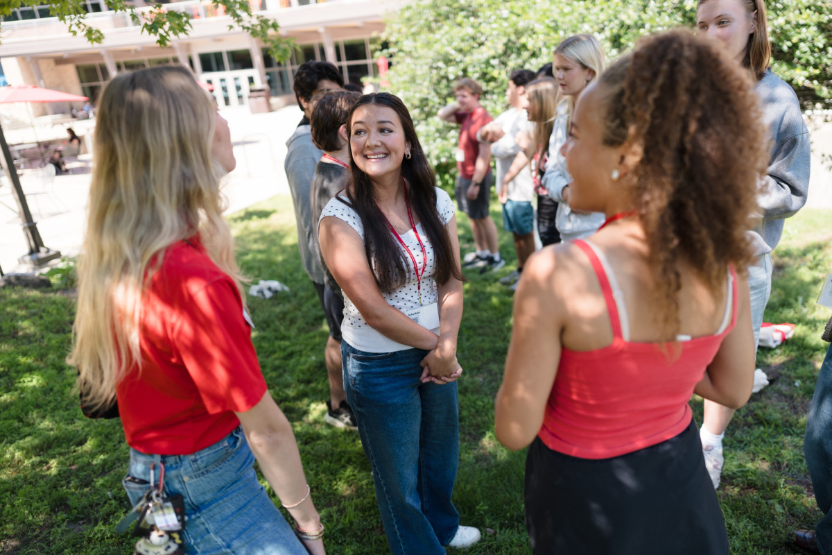 New UW–Madison students stand on the bright green lawn of a campus building and talk during a meet-and-greet session.