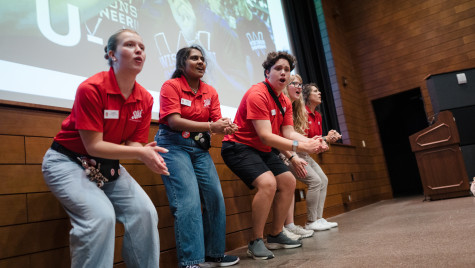 A row of students wearing bright Badger red shirts lead a room full of fellow students in a clapping chant.