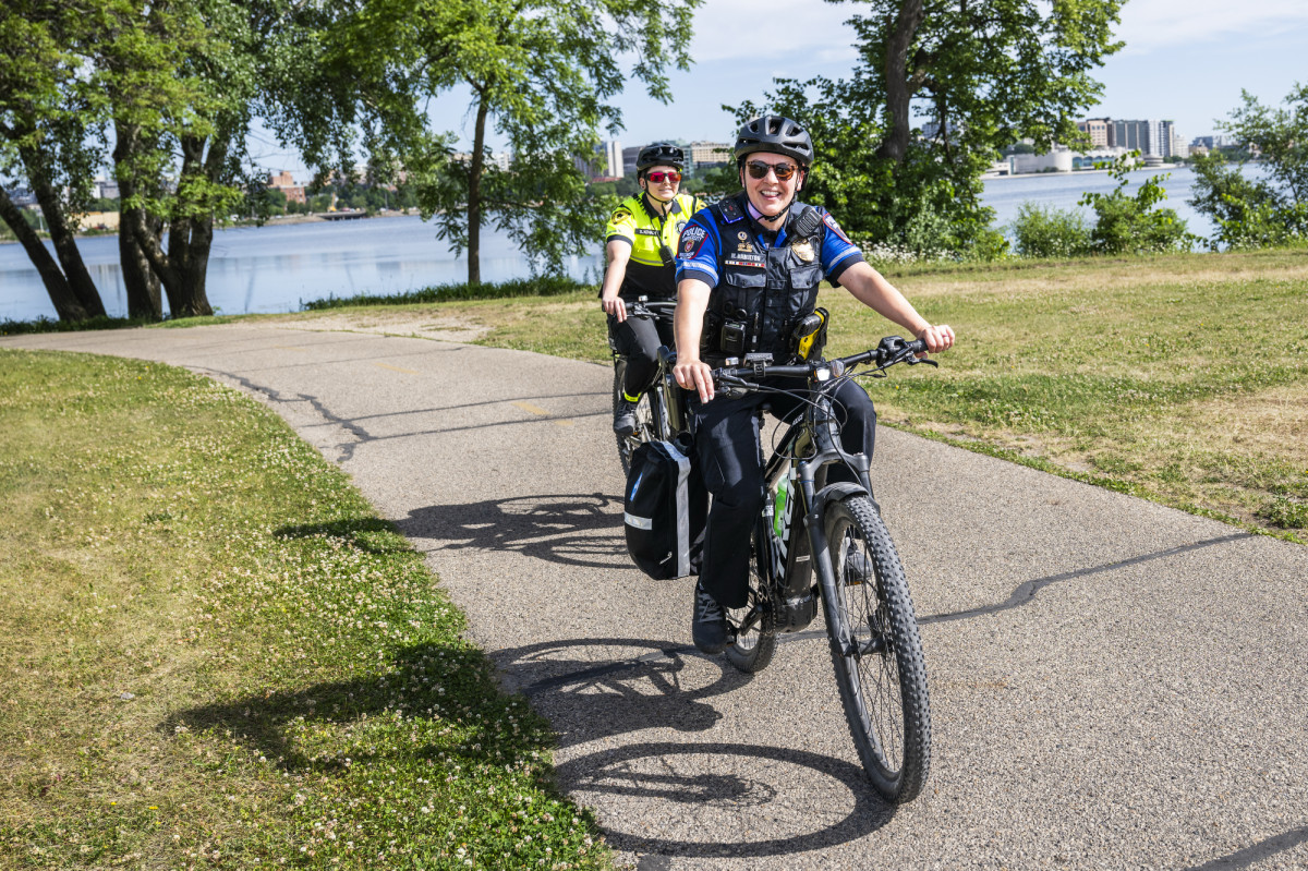 Meg Hamilton rides a black bicycle along a pathway with Lake Monona in the background.