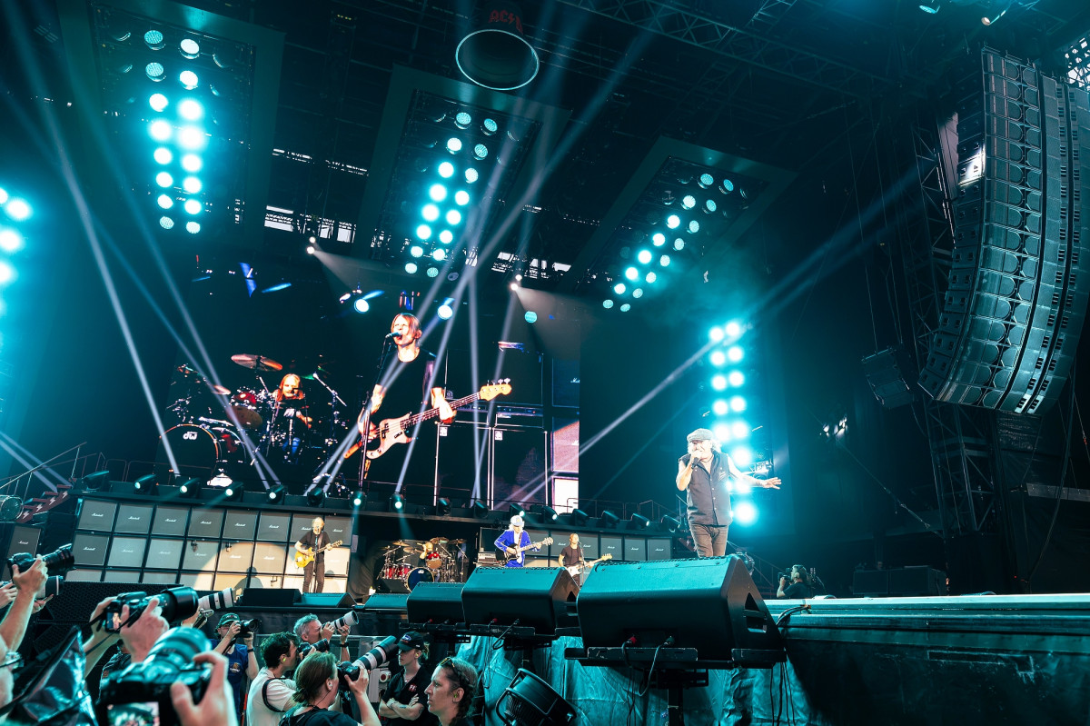 Johnson sings to the crowd on stage. Behind him a large screen shows close-up footage of the rest of the ACDC band.