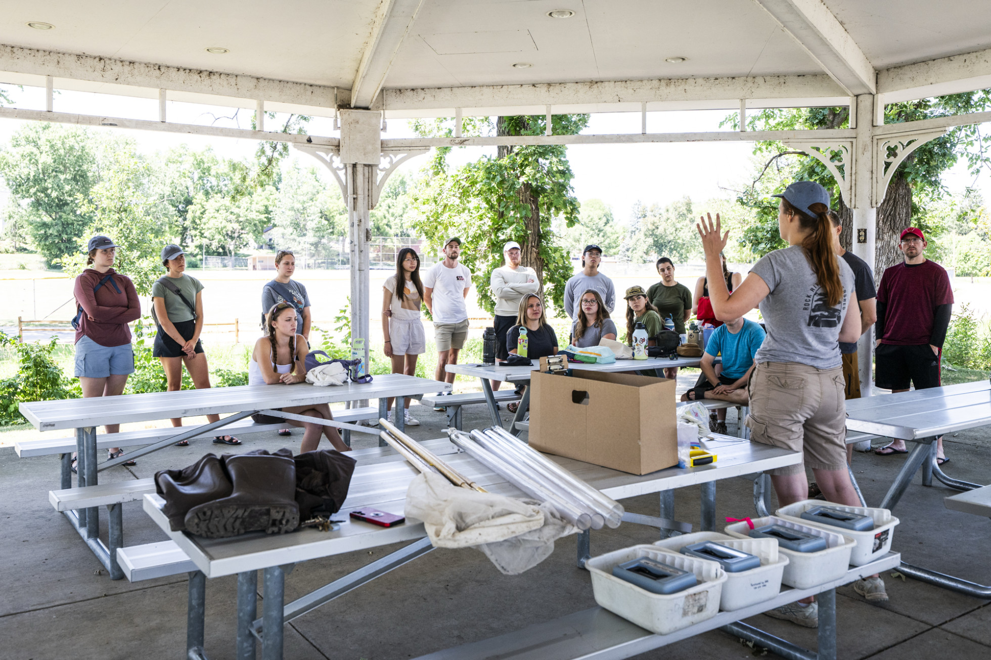 The class gathers under a gazebo and listens to a woman talking through details of the sample collection.