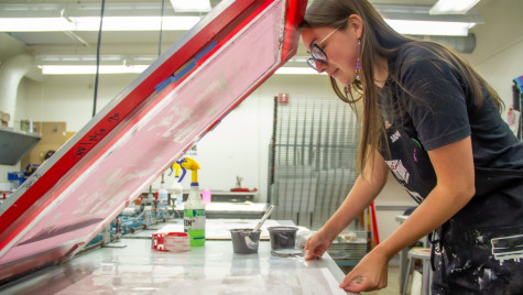 A student stands over a paper press.