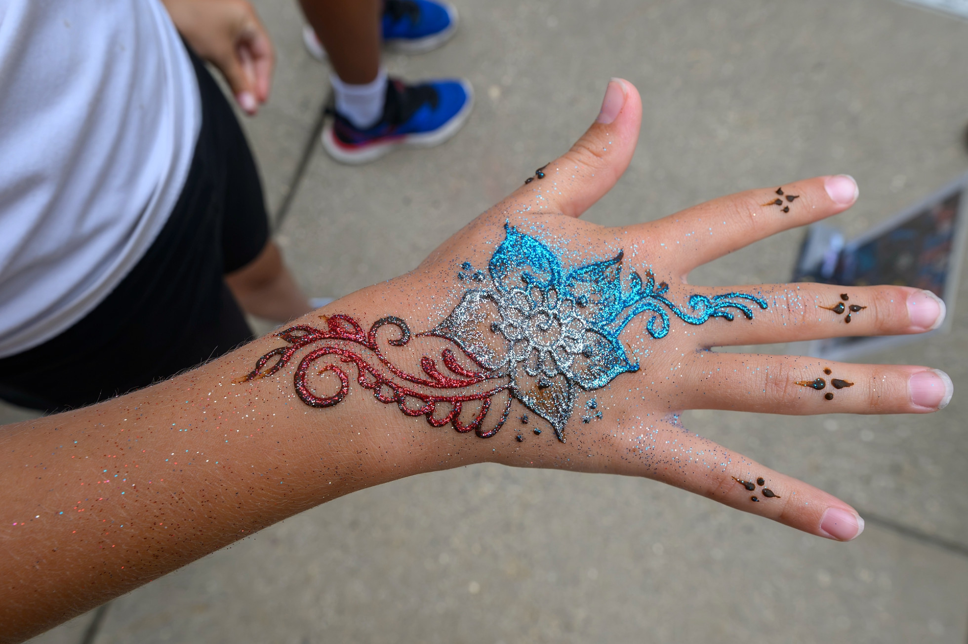 A close-up view of a hand displaying a sparkling glitter tattoo in red, white and blue.