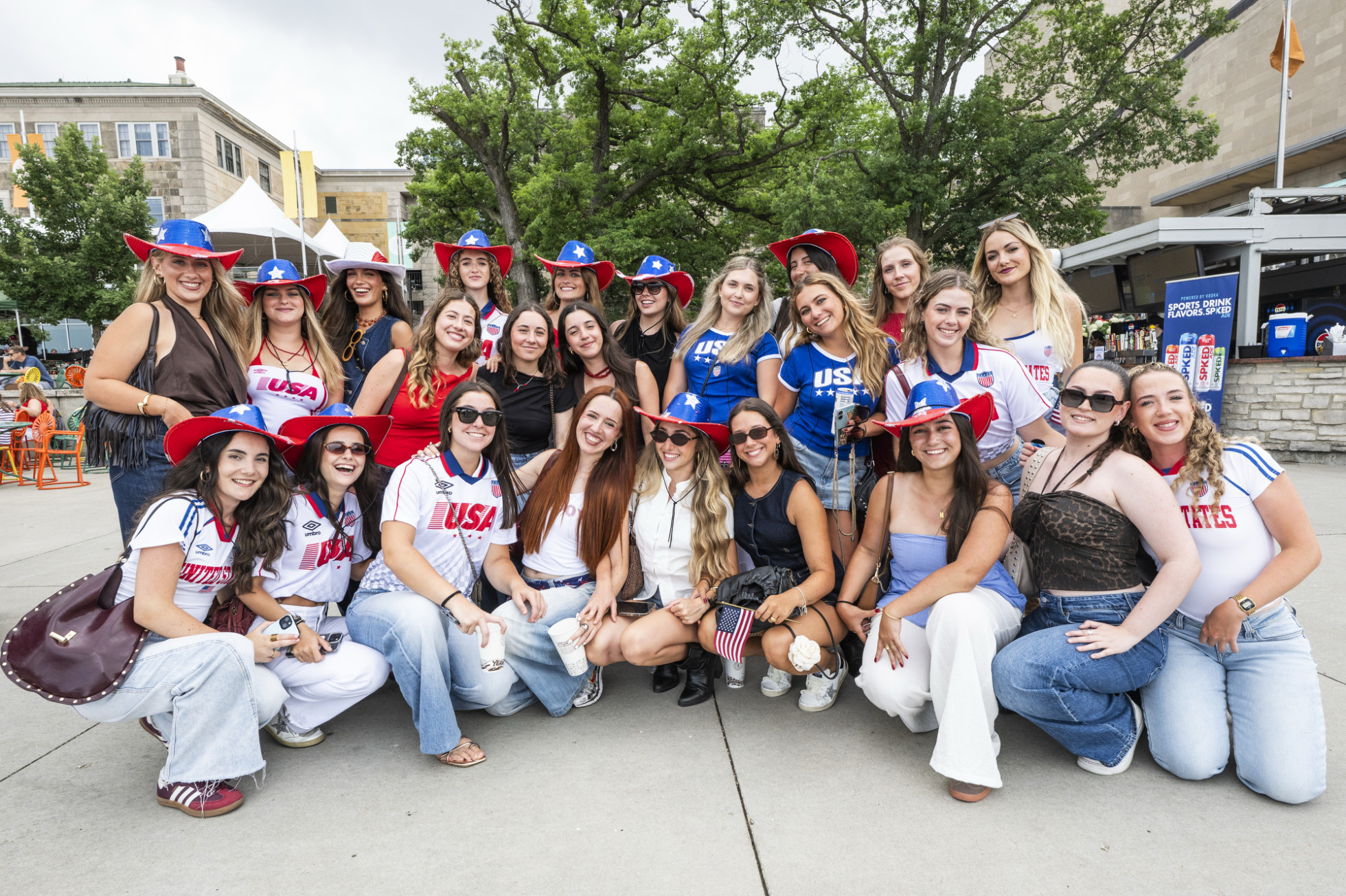 A group photo of women smiling and posing together on a concrete plaza. Many wear USA-themed apparel.
