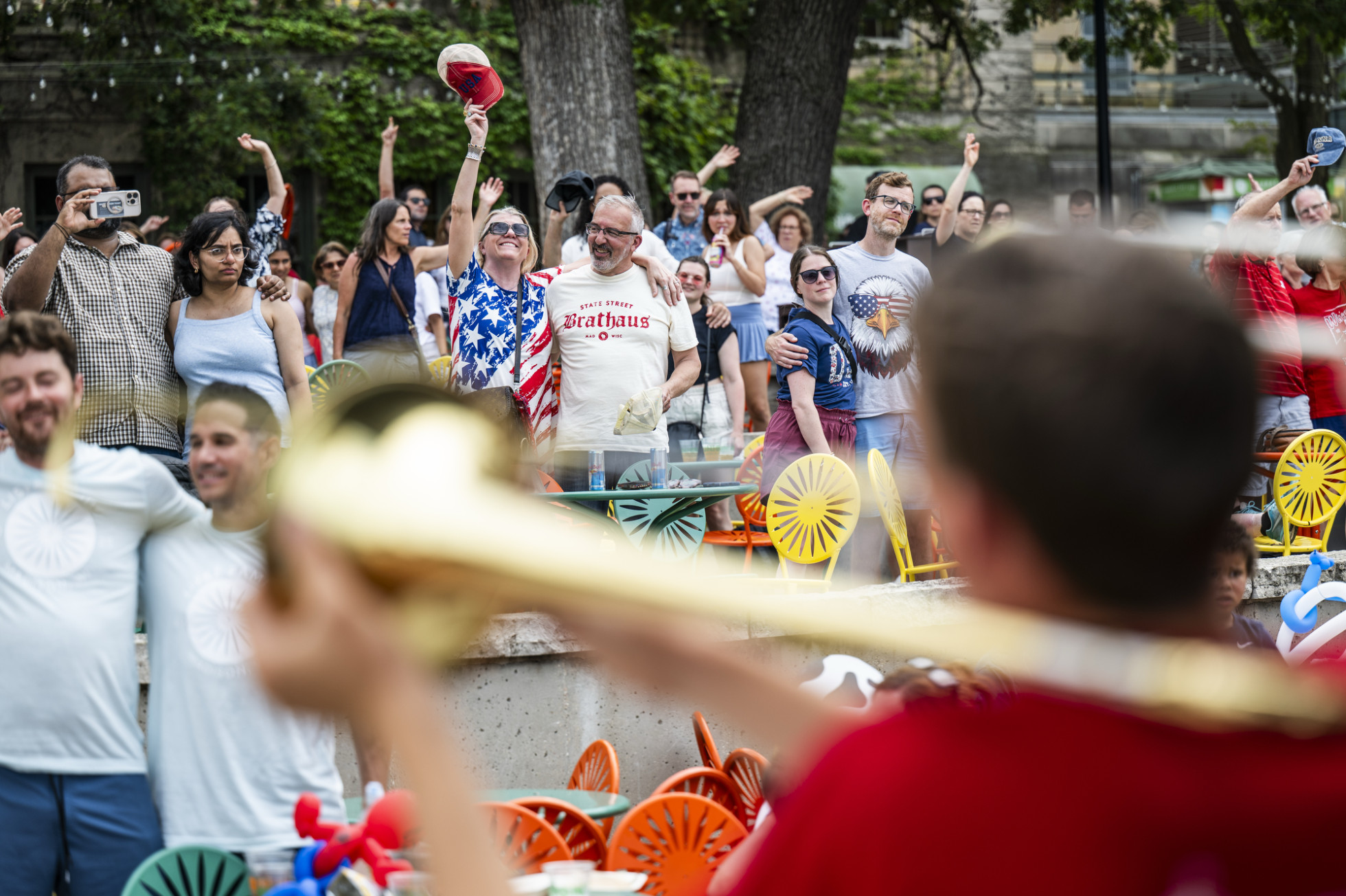 An over-the-shoulder photo looking past a brass instrument musician at an audience standing and waving.