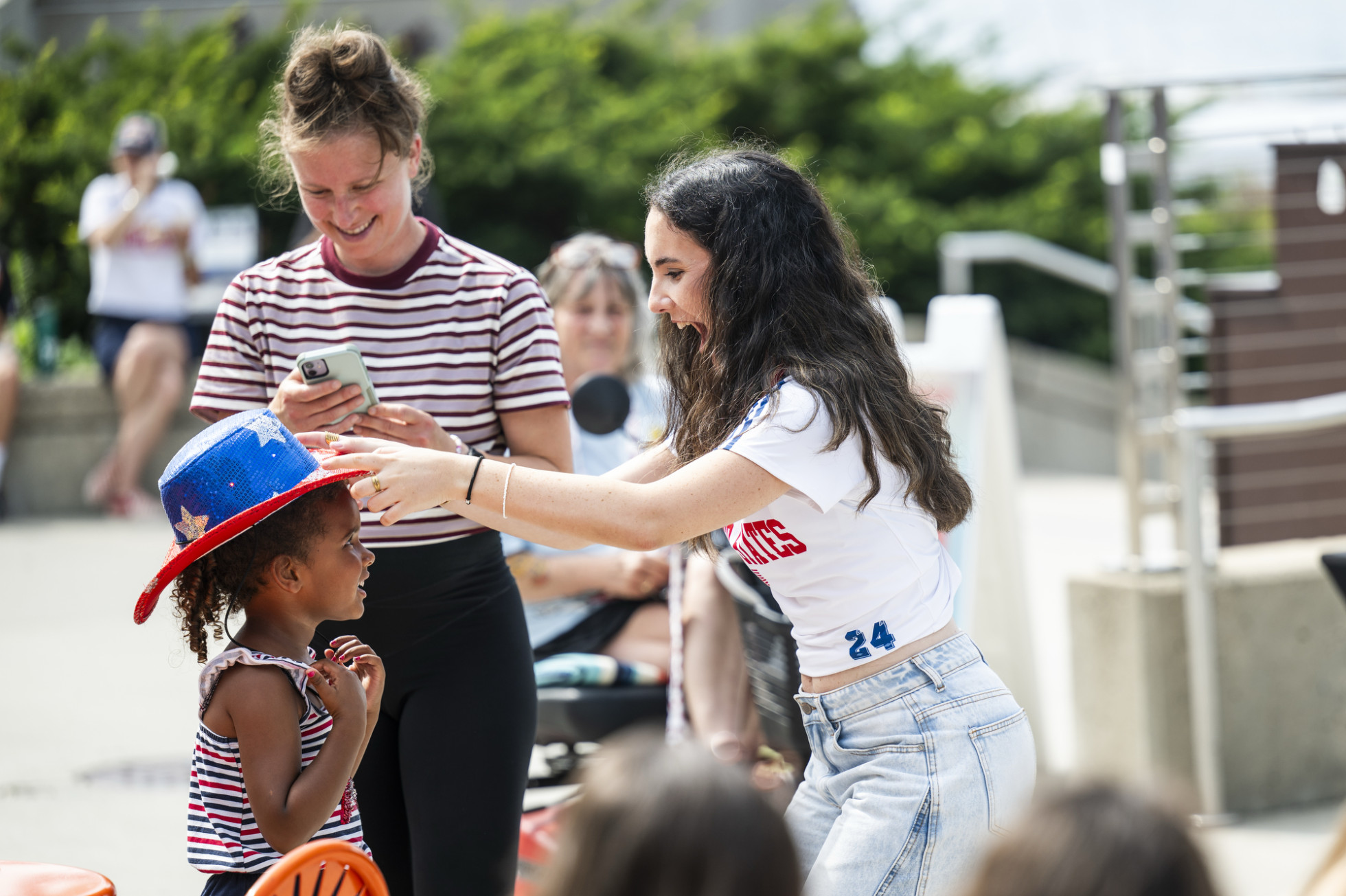A woman places a red, white and blue cowboy hat onto the head of a smiling girl.
