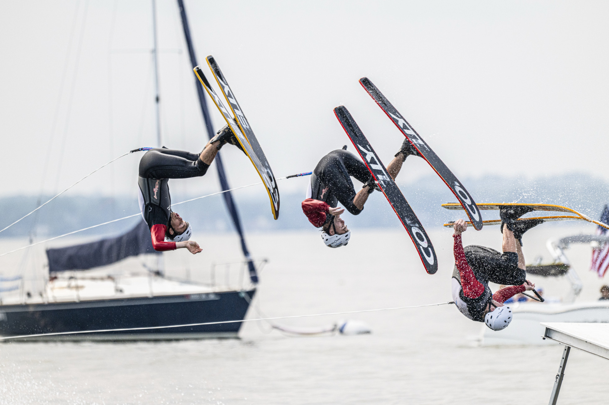 Three water skiers execute synchronized mid-air backflips over a lake. 