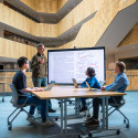 Students at tables listen to a speaker in front of a projection screen with text from a research study.