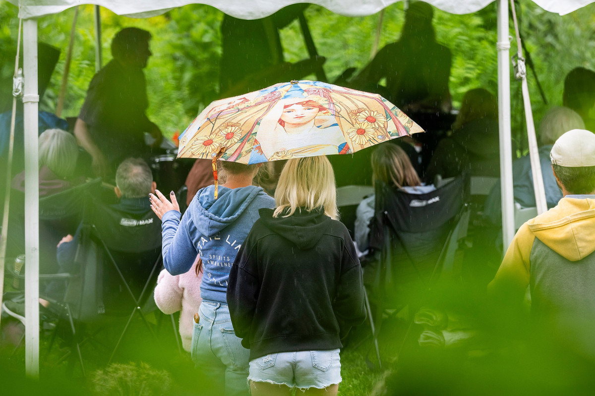 Audience members listening to the jazz trio, Mr. Chair huddle under an umbrella