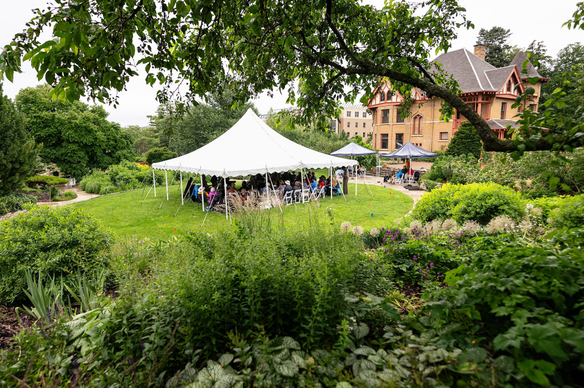 People gather under a large tent at the center of a green space at Allen Centennial Gardens