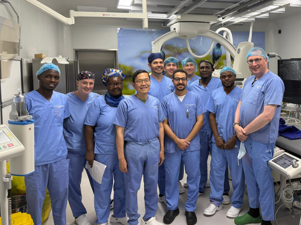 A group of doctors wear blue scrubs and stand together for a photo in front of a large xray machine.