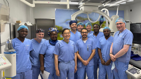 A group of doctors wear blue scrubs and stand together for a photo in front of a large xray machine.