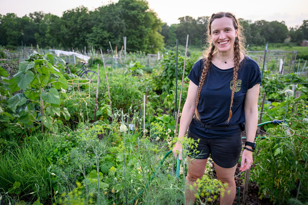 A woman with two long braids smiles in front of a large garden