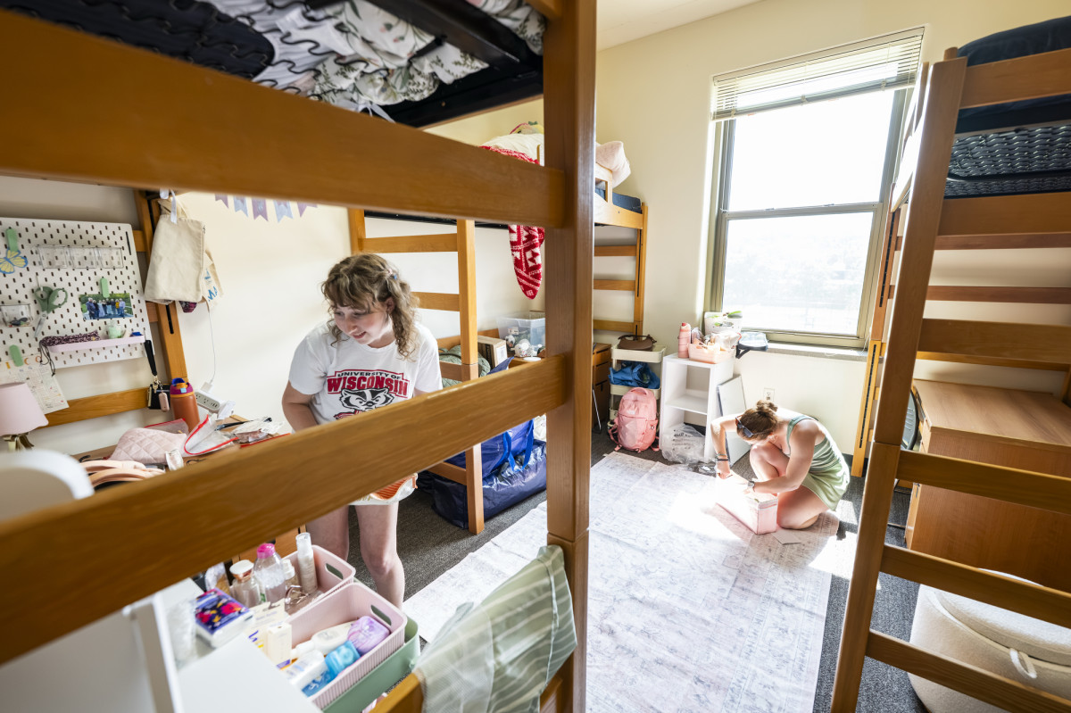 Two students simultaneously work to decorate respective spaces in a shared residence hall room.