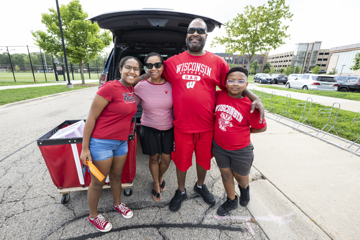 A family, all wearing Badger red shirts, pose for a photo outside of their car.