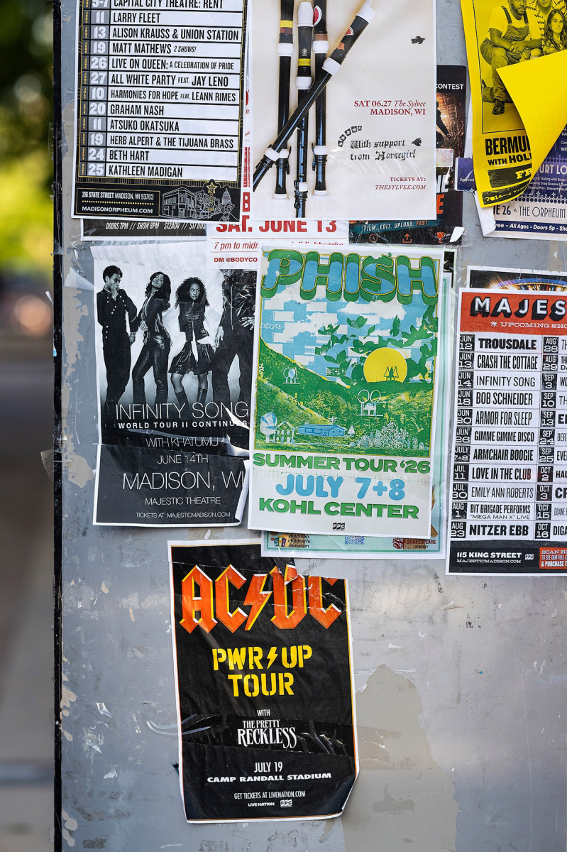 Flyers for different summer concerts in Madison, including AC/DC and Phish cover a state street bulletin board.