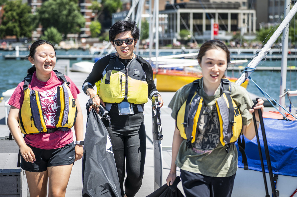 Three people wearing life jackets get ready to board a boat