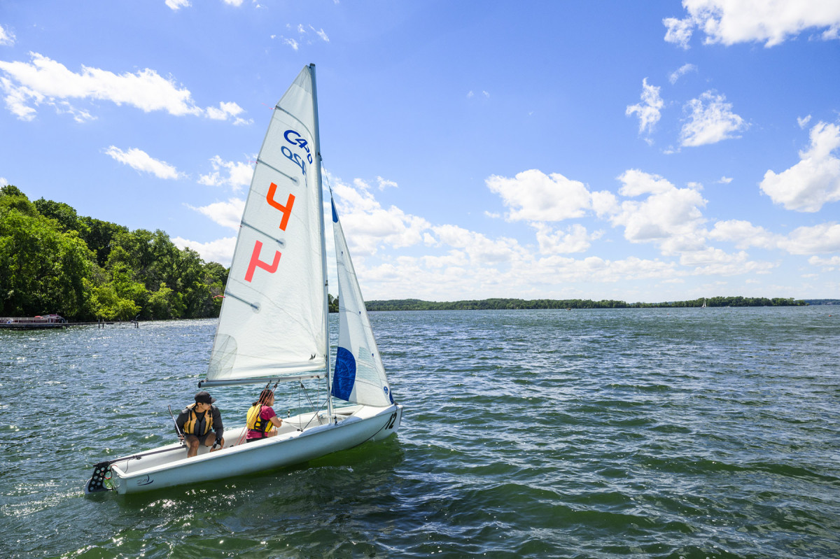 Two people in a Hoofers sailboat on Lake Mendota against a blue sky