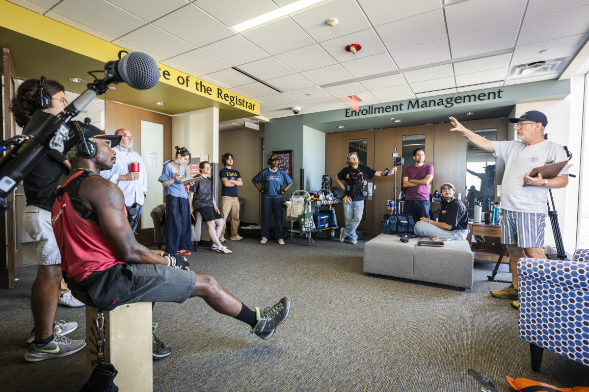Large office interior with film crew looking a person giving direction