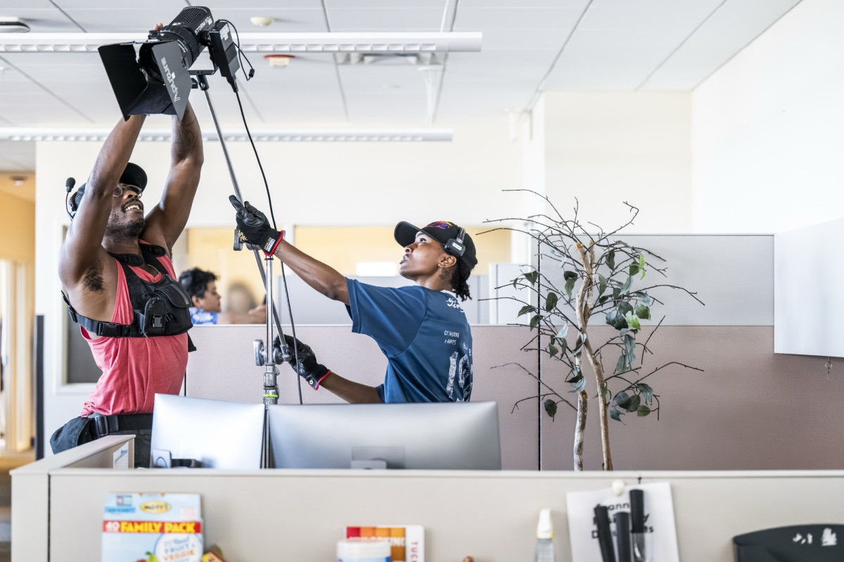 Two people working together to set up a light for filming inside of an office setting