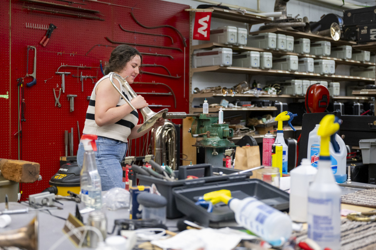 A student staff member fixes an instrument in a workshop setting.