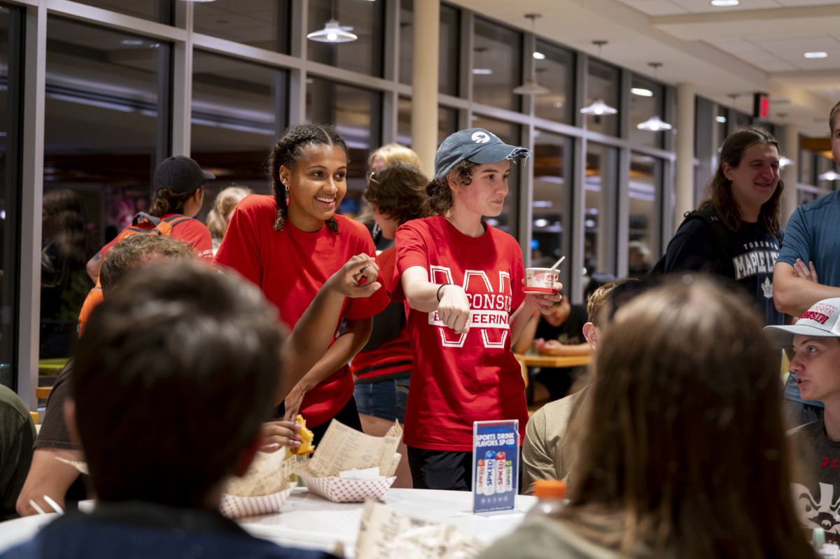Band members interact cheerfully with a group seated around a table indoors. 