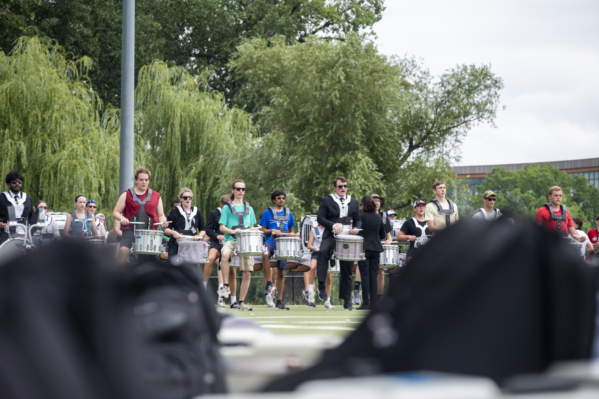 A row of drummers practice on a turf playing field.